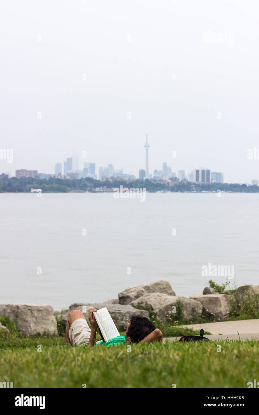 Mann auf den Rasen legen und lesen Sie ein Buch mit einem Toronto Skyline im Hintergrund Stockfoto