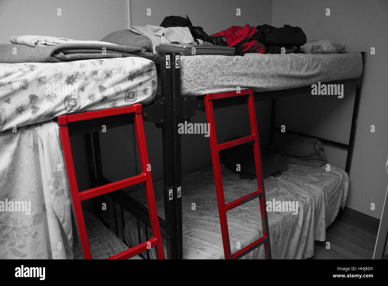 Black And White Hostel Schlafsaal mit Etagenbetten - rot gefärbten Leiter und Jacke hervorgehoben Stockfoto