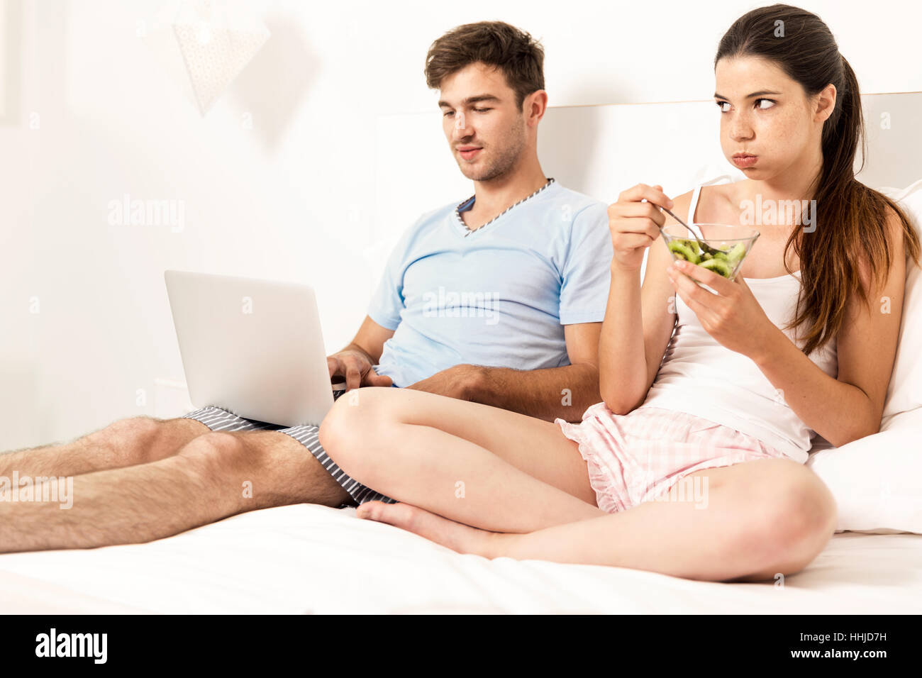 Süchtig junge Mann auf dem Bett mit einem Laptop, während die Frau wütend sieht Stockfoto