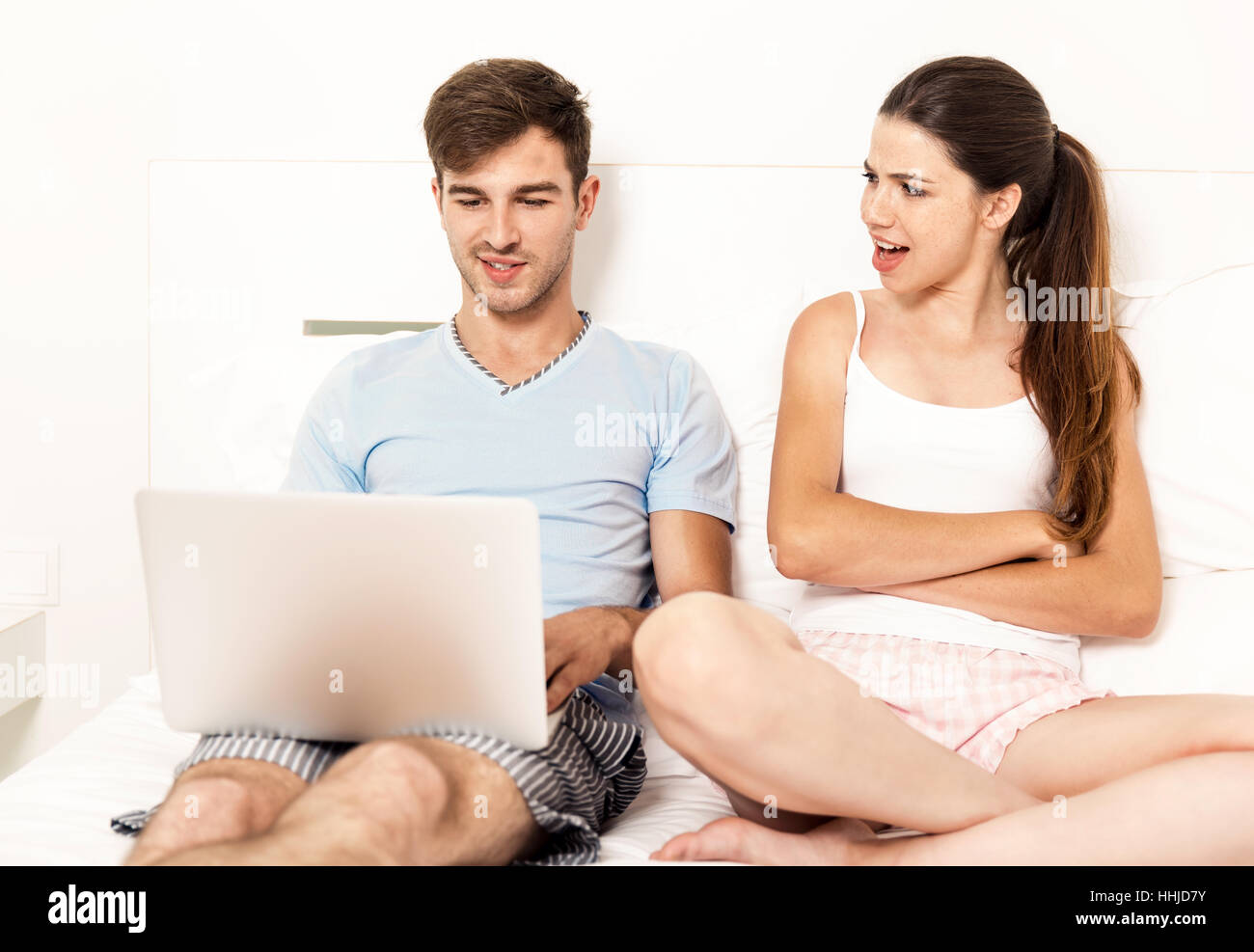 Süchtig junge Mann auf dem Bett mit einem Laptop, während die Frau wütend sieht Stockfoto