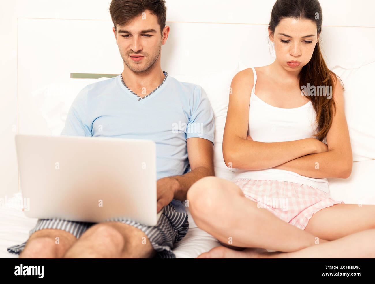 Süchtig junge Mann auf dem Bett mit einem Laptop, während die Frau wütend sieht Stockfoto