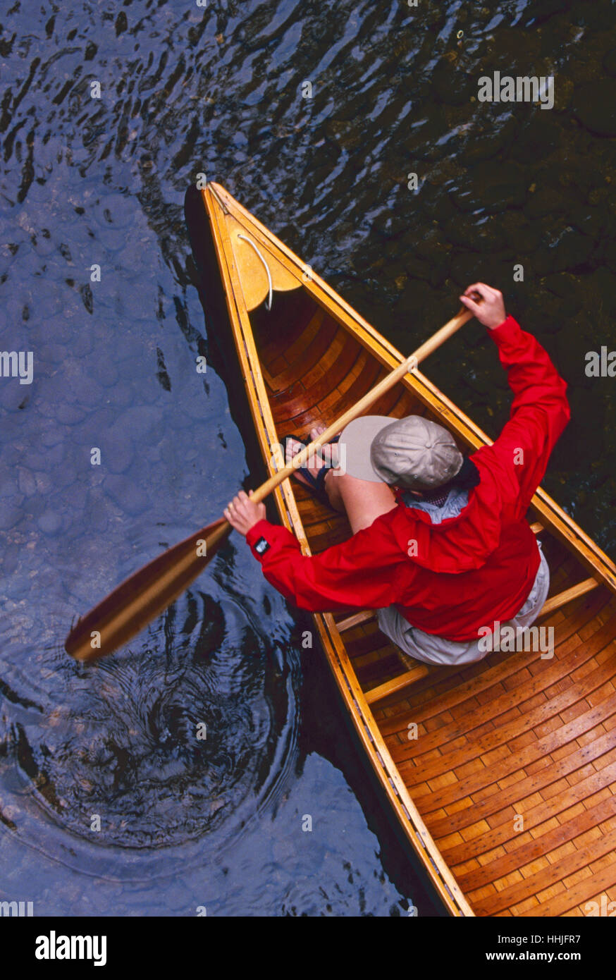 Eine junge Frau in ihrem 20 tragen eine leuchtende rote Jacke paddelt ihr Vintage Holz Kanu in einem Wildwasser-stream Stockfoto