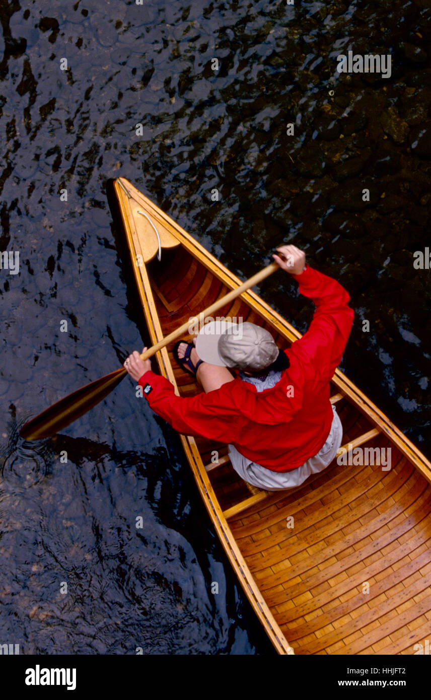 Eine junge Frau in ihrem 20 tragen eine leuchtende rote Jacke paddelt ihr Vintage Holz Kanu in einem Wildwasser-stream Stockfoto