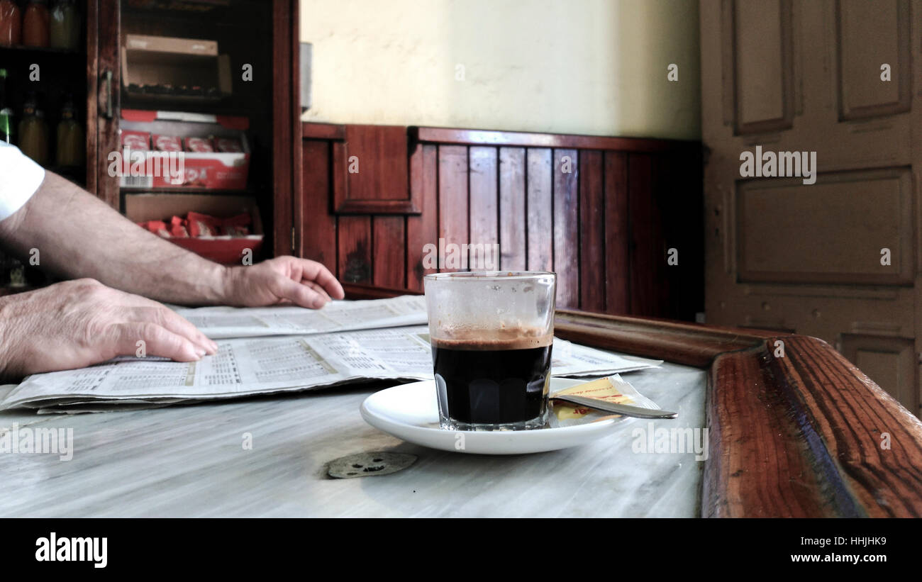 Alter Mann liest eine Zeitung mit seinen Händen, mit einem Kaffee auf das Glas, allein in seinem eigenen Vintage Bar, Las Palmas, Spanien. Stockfoto