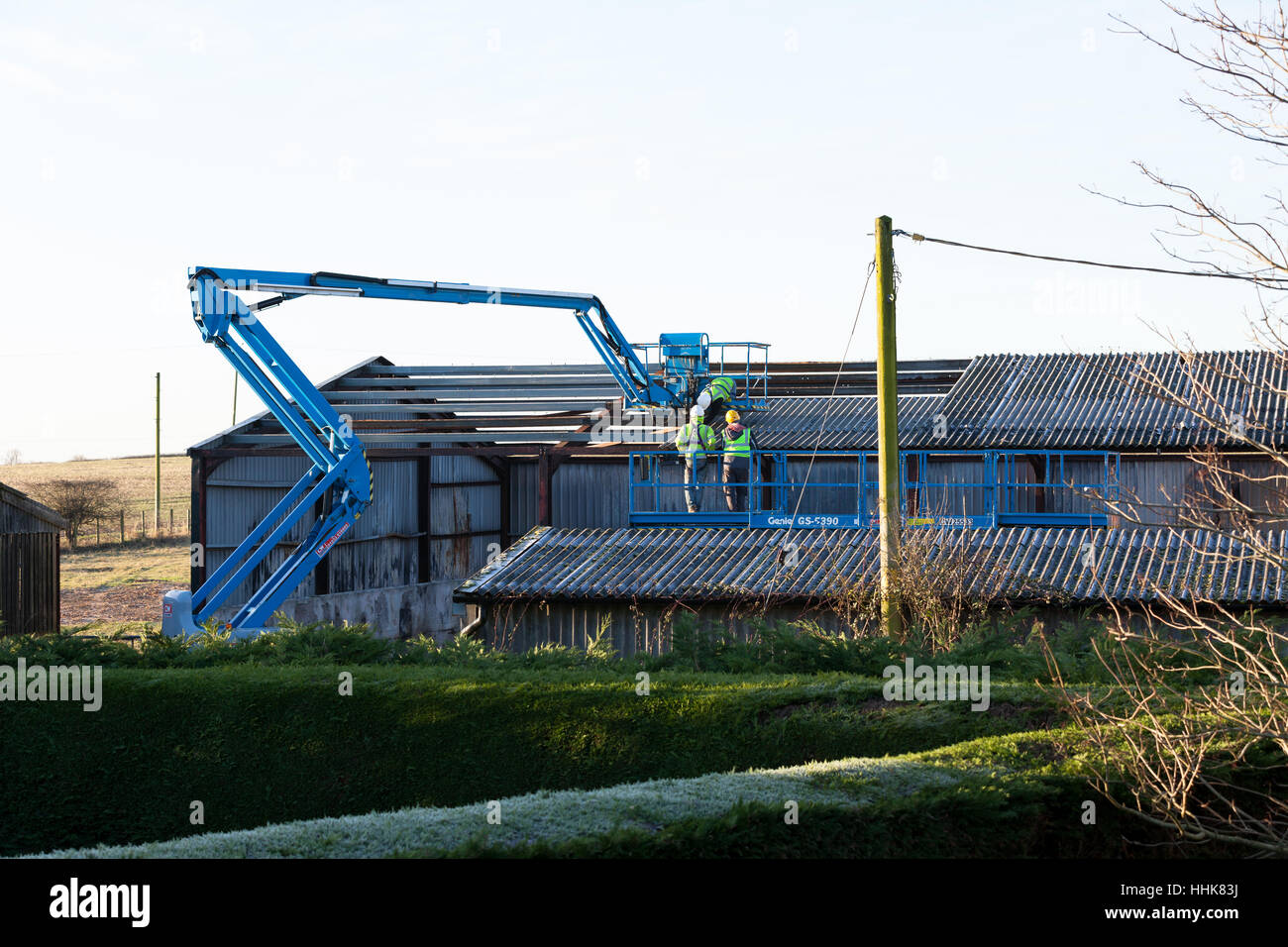 Gruppe von 3 männliche Arbeitnehmer mit hardhats und Warnwesten auf hydraulischen Aufzug in Vorbereitung der Reparatur zu stalldach, Großbritannien Stockfoto