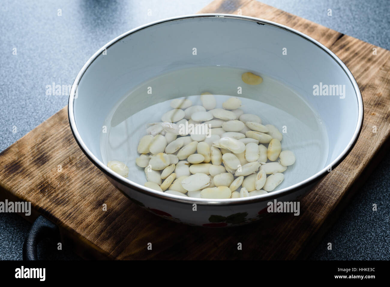 Große weiße Bohnen einweichen in Wasser auf ein dunkles Holz Schneidebrett. Stockfoto