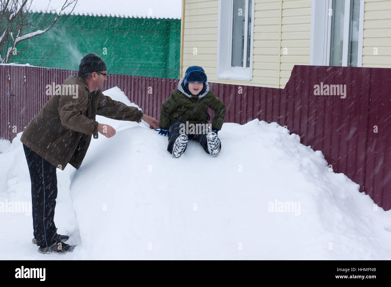 ein kleiner Junge reitet auf einem schneebedeckten Hügel in der Obhut der Großeltern Stockfoto