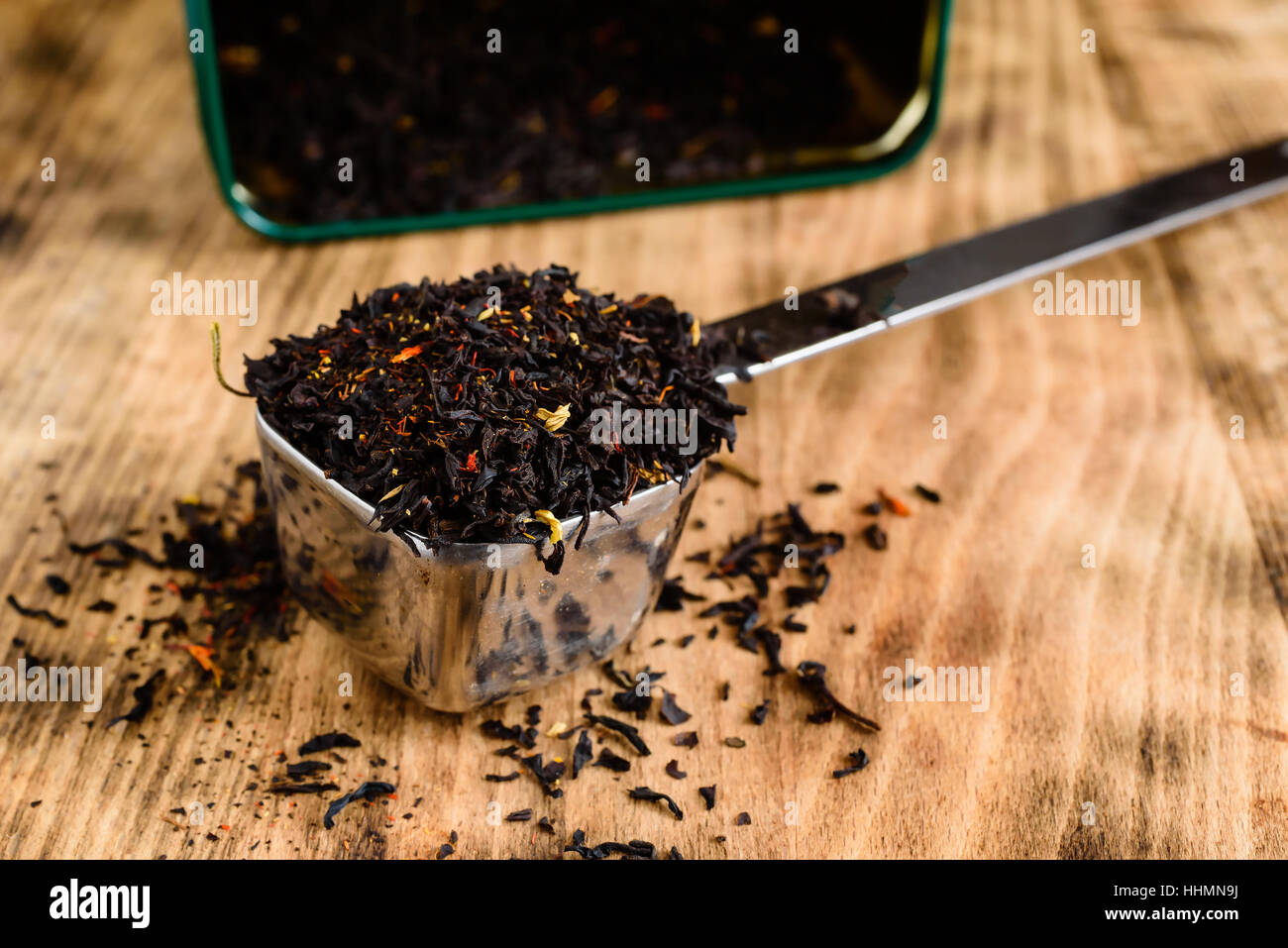 Aromatisierter Tee in Metall Kugel auf Holzbrett. Offener Tee Teedose im Hintergrund. Stockfoto