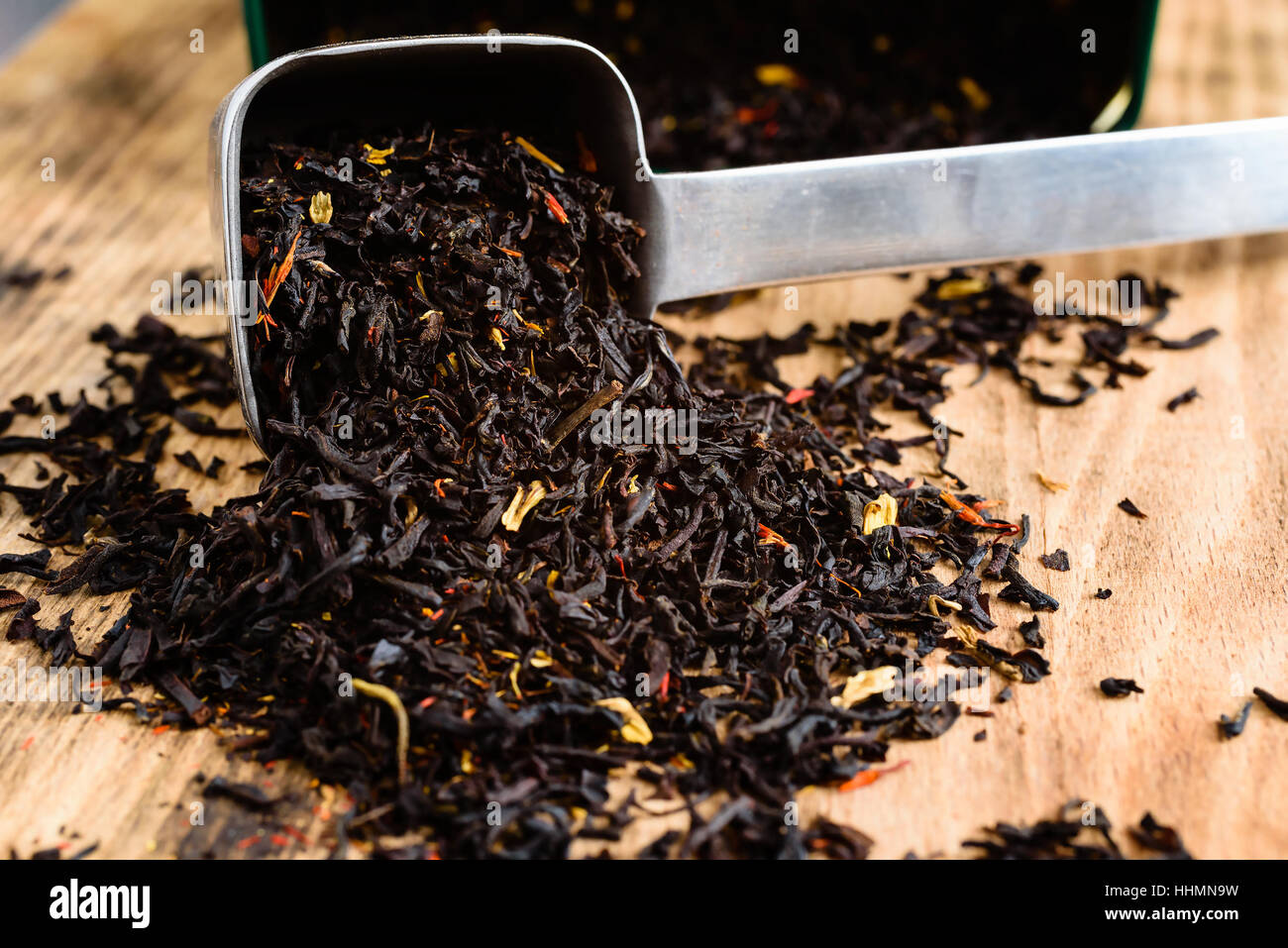 Aromatisierter schwarzer Tee aus Metall Kugel auf Holzbrett. Offener Tee Teedose im Hintergrund. Stockfoto