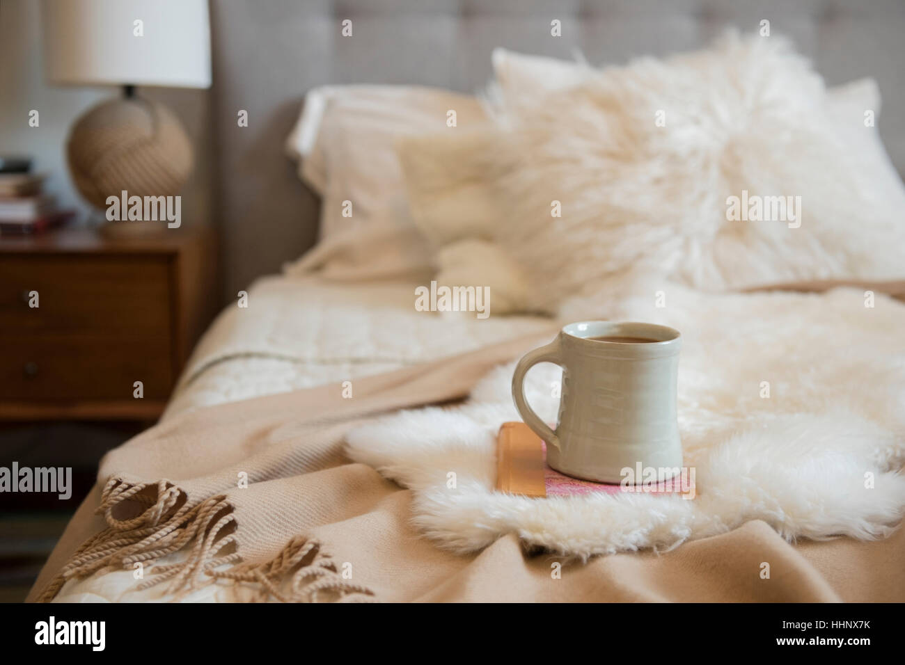 Kaffeetasse und Buch über Fell auf Bett Stockfoto