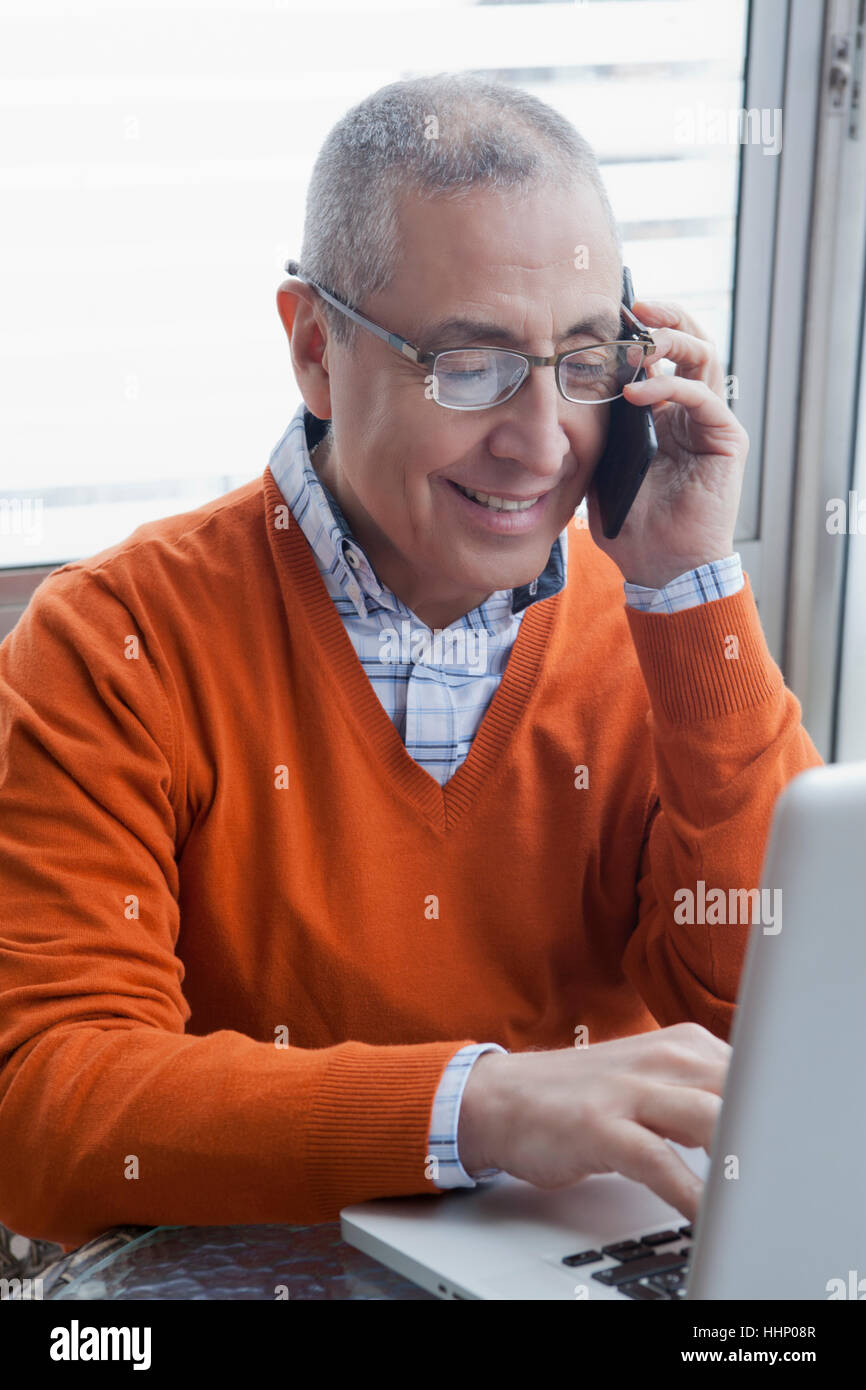 Lächelnder Hispanic Mann Multi-tasking mit Handy und laptop Stockfoto