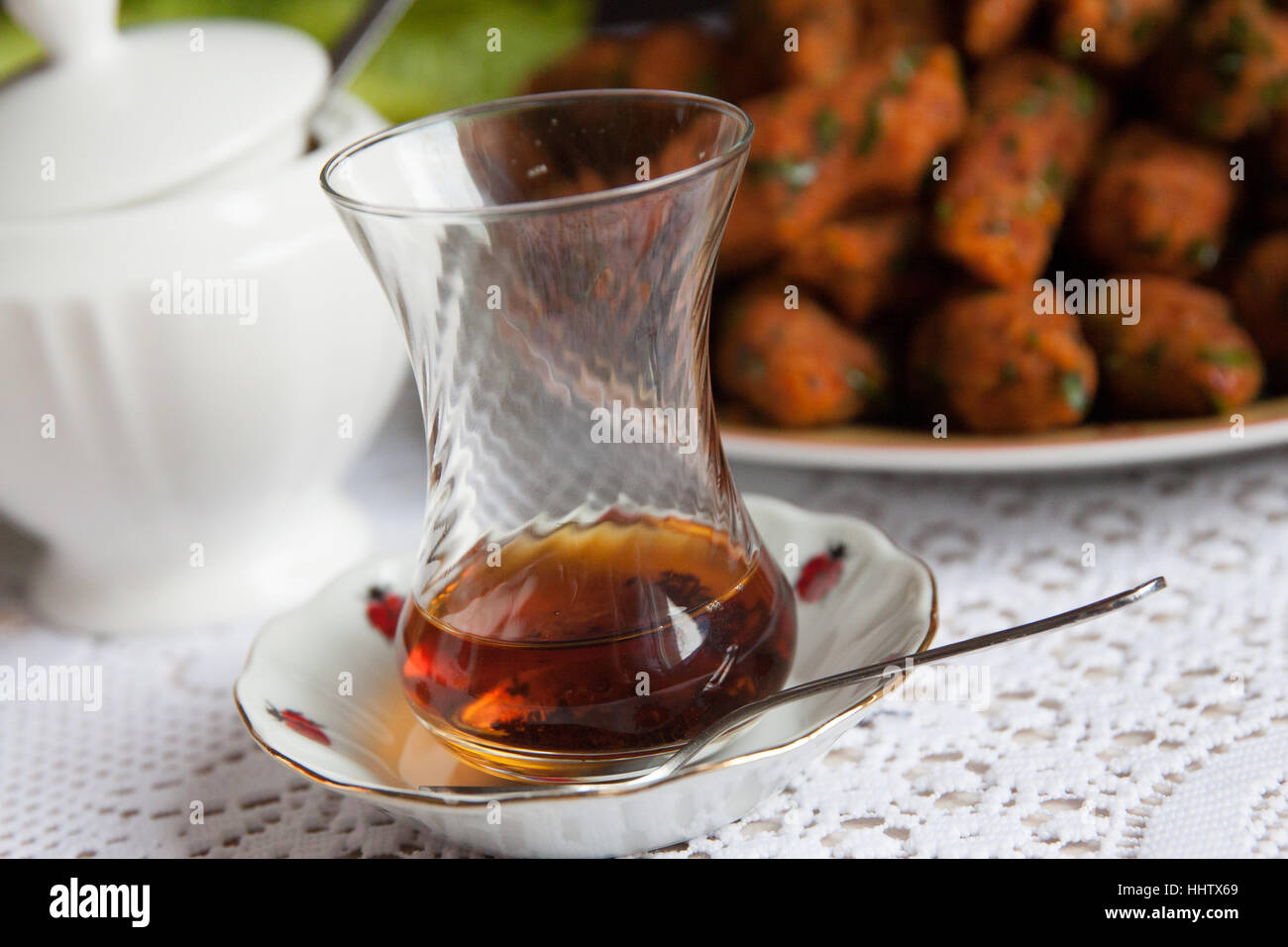 Türkischer Teeglas halb mit schwarzem Tee, mit Essen und Zucker voll kann im Hintergrund. Stockfoto