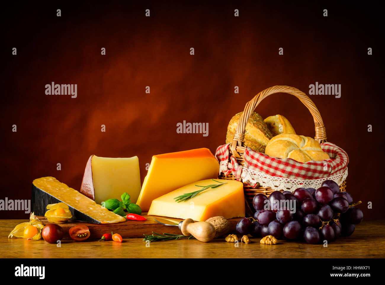 Harter Käse Gauda, Cheddar und Edam mit Korb Brötchen und Trauben Stockfoto