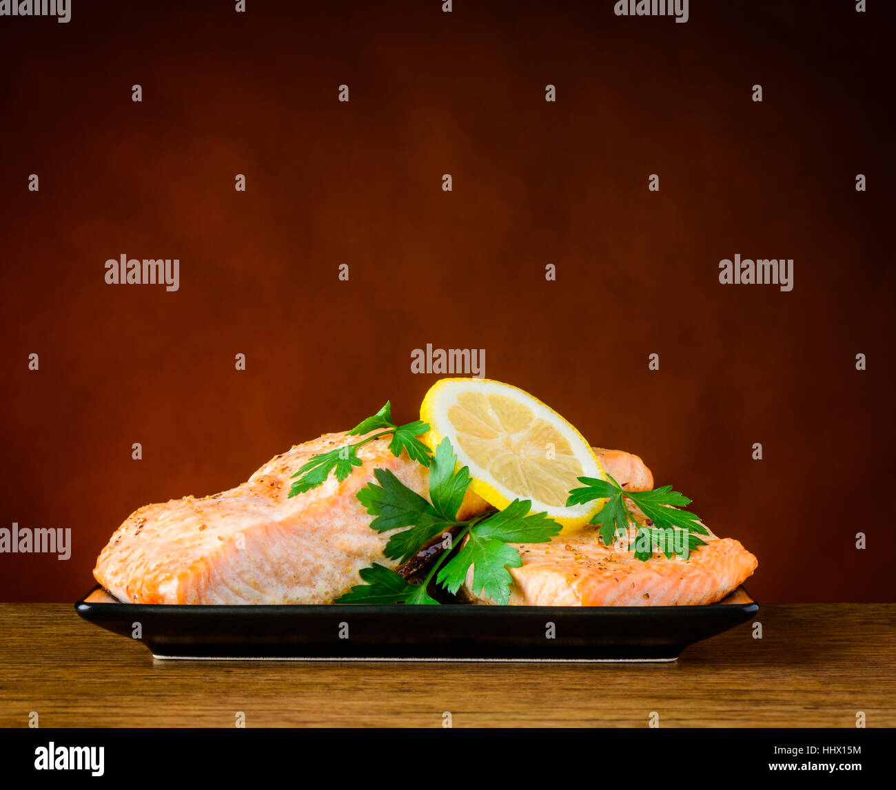 Colse-Up von gekocht Lachs Fisch-Filet mit Petersilie und in Scheiben geschnittene Zitrone auf einem dunklen Teller Stockfoto