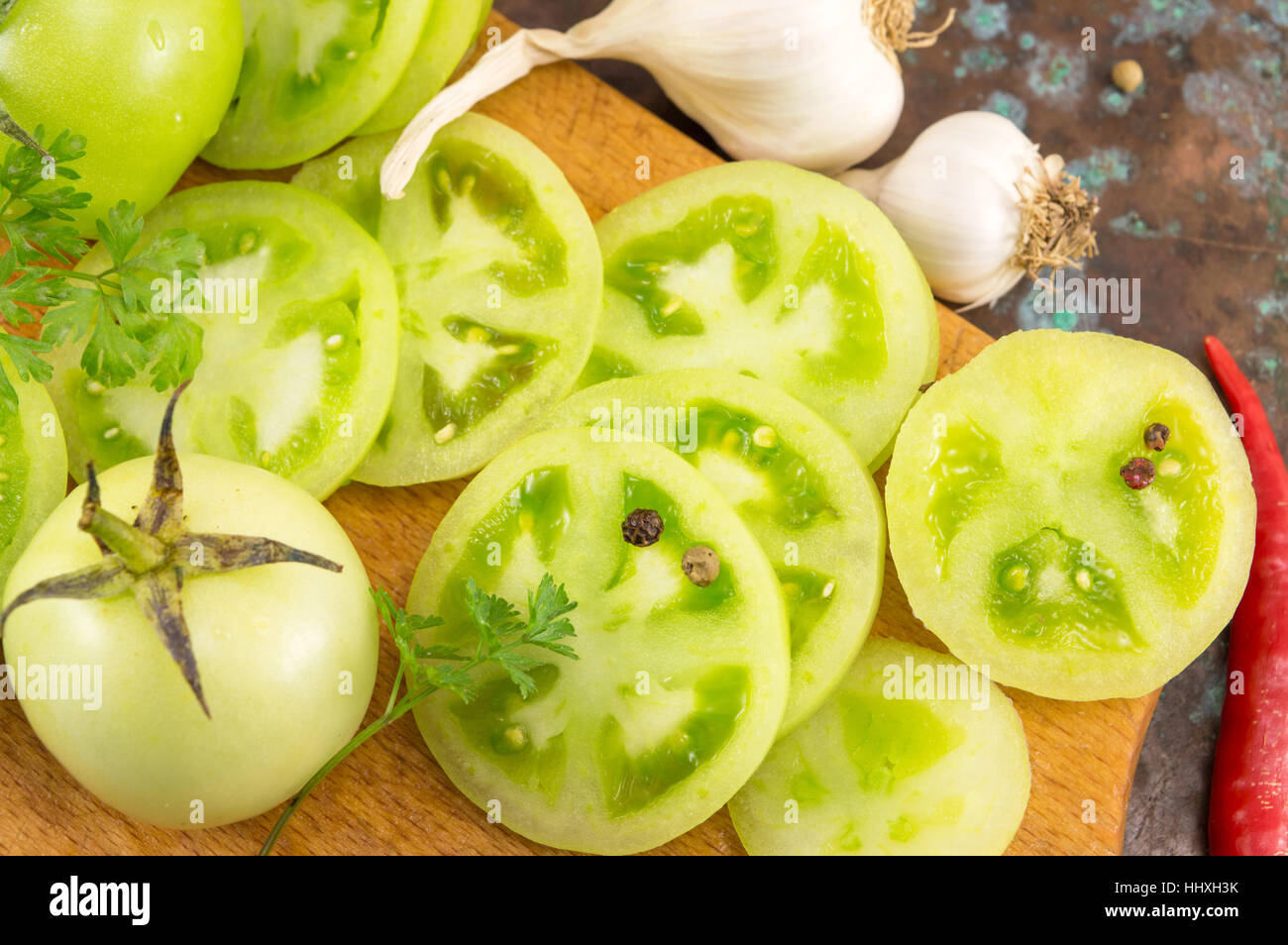 grüne Tomaten mit Knoblauch und Paprika auf einem Holzbrett Stockfoto
