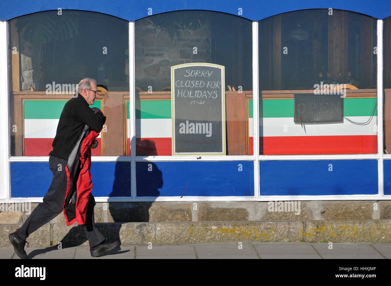 Ein Mann in Eile, vorbei an einem Café geschlossen für den Winter in Cornwall. Stockfoto