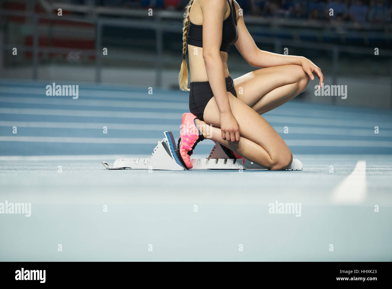 Weibliche Läufer kniet am Startblock am Sportplatz Stockfoto