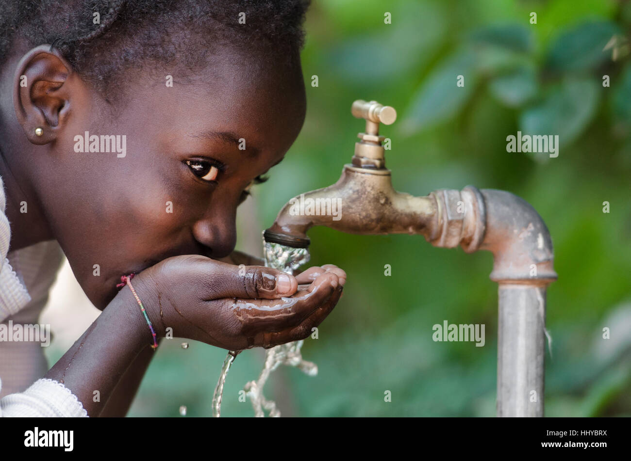Schöne afrikanische Kind trinken aus einem Hahn (Wasser-Knappheit-Symbol). Afrikanische Mädchen trinken Wasser aus einem Hahn. Wasser aus einem Hahn in t gießen Stockfoto