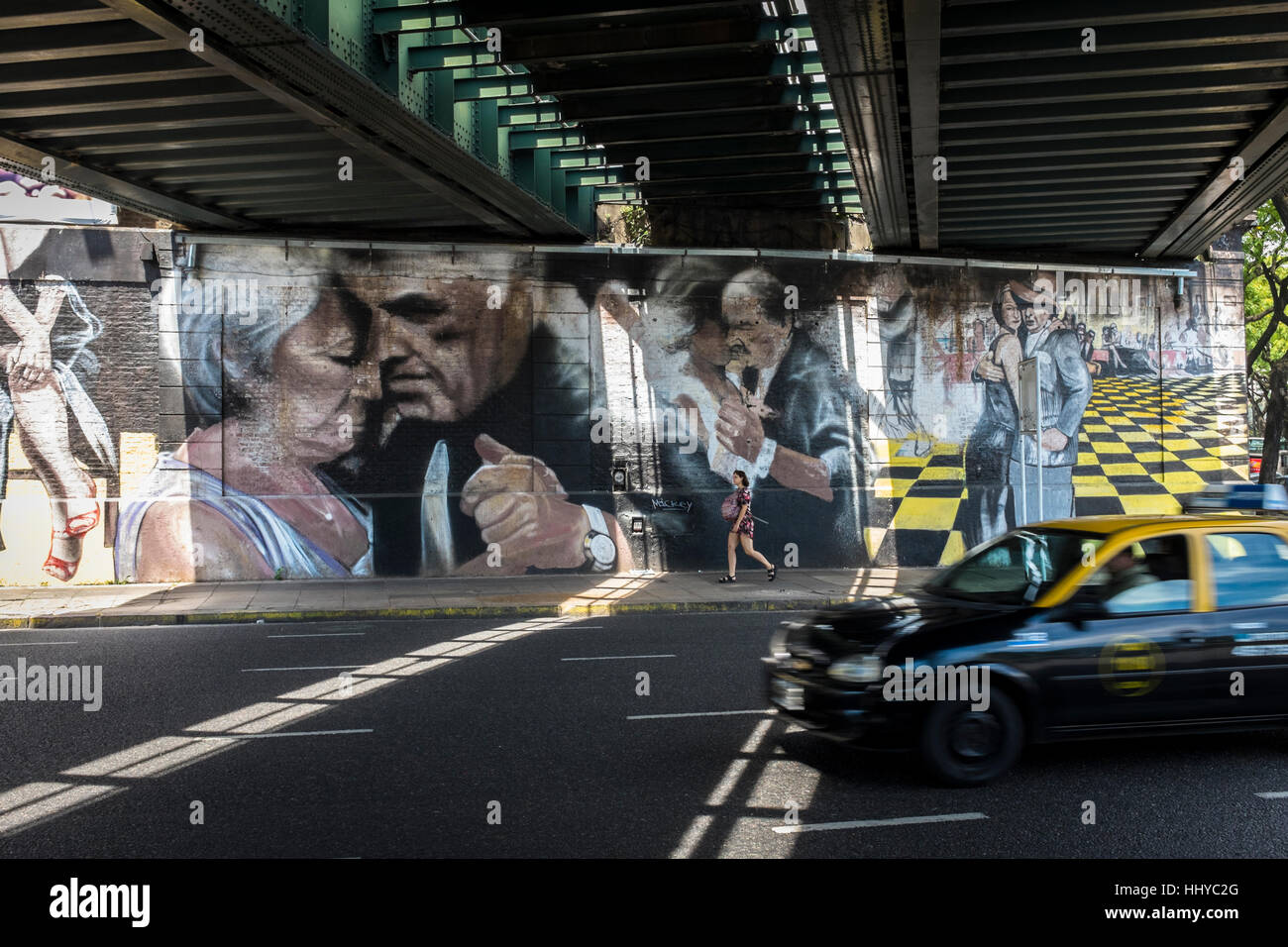 Ein Taxi fährt unter einer Eisenbahnbrücke wo gestrichene Wände zeigen drei Paare tanzen Tango in der Stadt Buenos Aires, Argentinien. Stockfoto