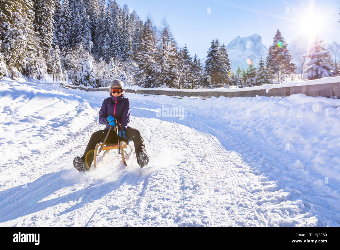Fröhliches Mädchen reitet einen Schlitten bergab auf einer Schnee bedeckten Schlitten Trail in einer weißen sonnigen Winter Berglandschaft Stockfoto Fröhliches Mädchen reitet einen Schlitten bergab auf einer Schnee bedeckten Schlitten Trail in einer weißen sonnigen Winter Berglandschaft Stockfoto