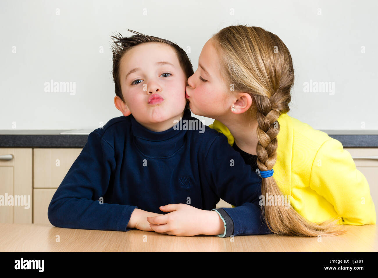Hübsches junges Mädchen küsst ihren kleinen Bruder ein zu Hause in der Küche Stockfoto