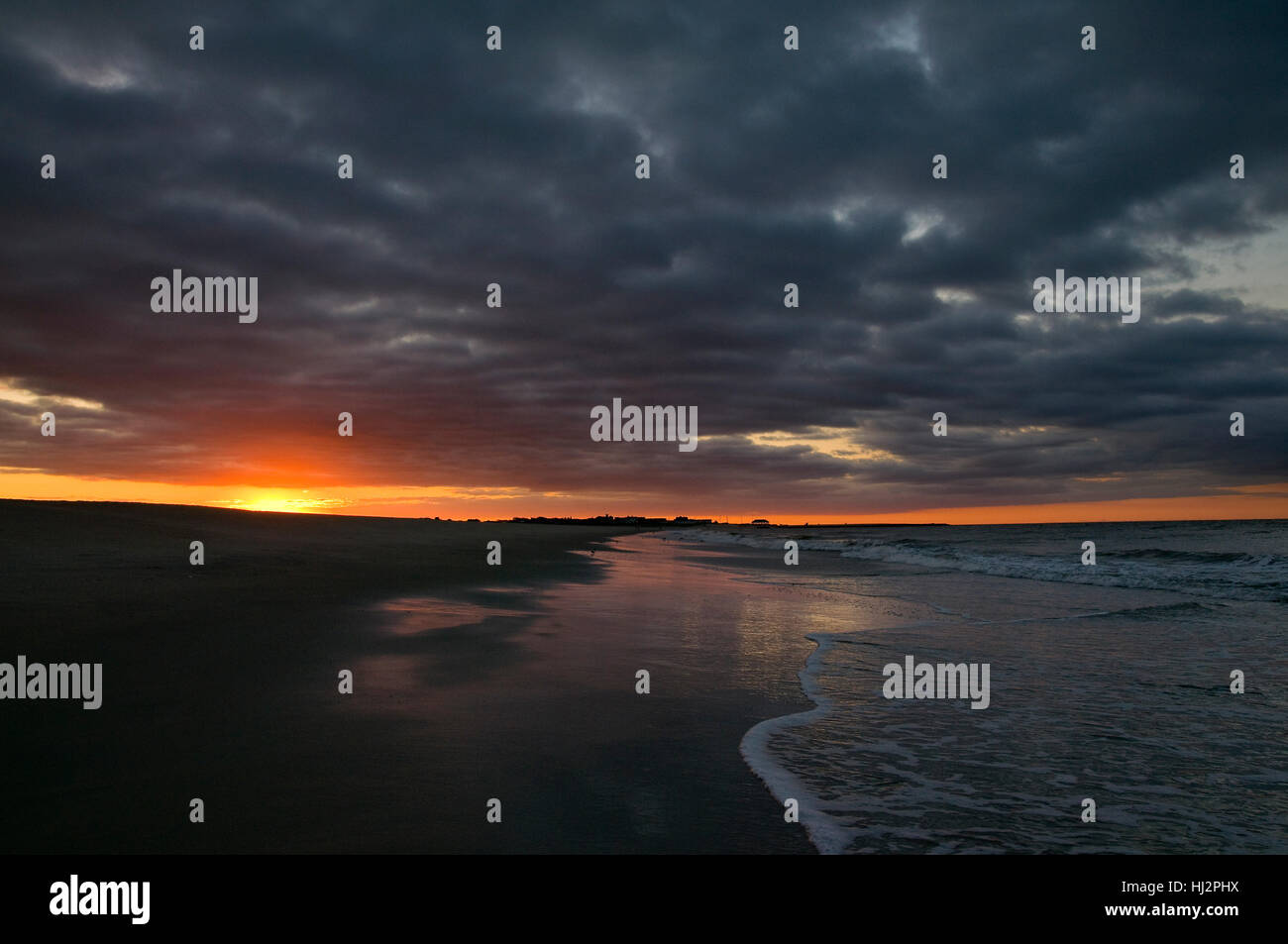 Die Sonne geht unter einem stark bewölktem Himmel auf dem sandigen Strand. Stockfoto