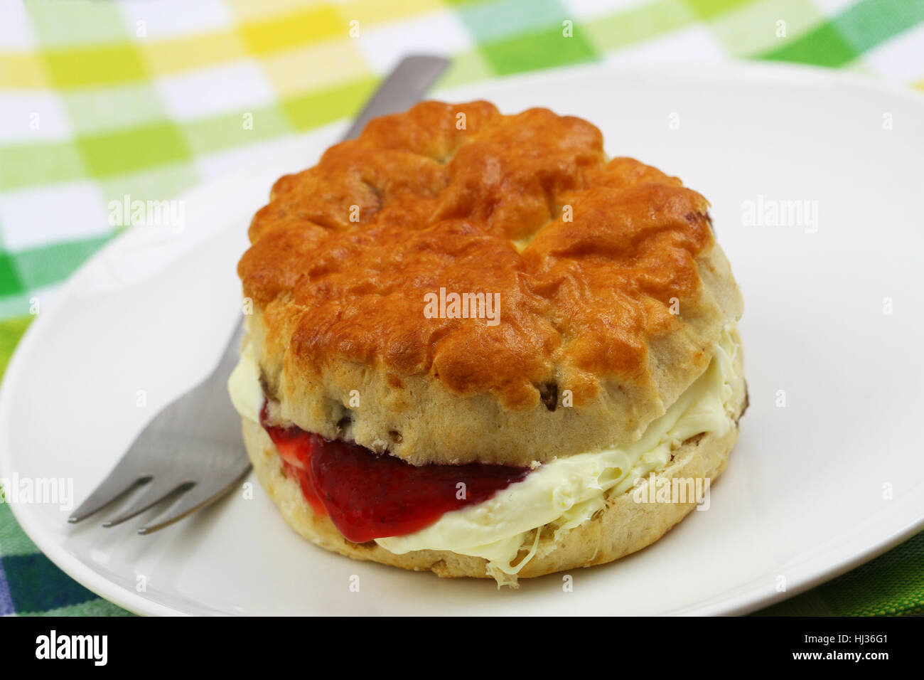 Frisch gebackenen englischen Scone mit traditionellen Clotted Cream und Erdbeermarmelade auf weißen Teller, Nahaufnahme Stockfoto