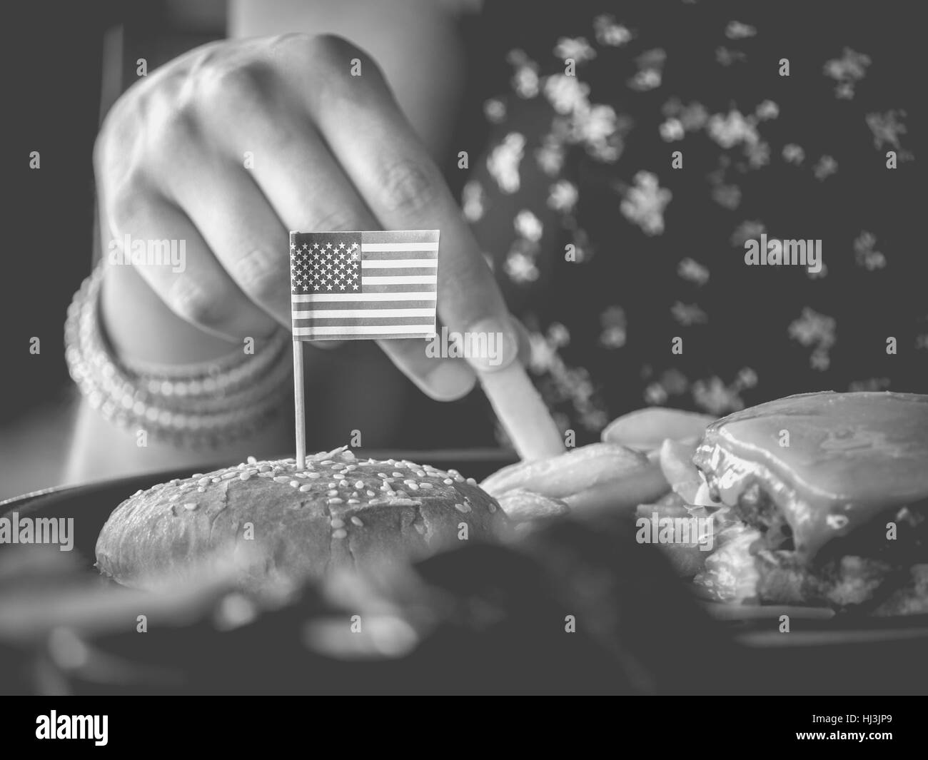 Weibliche Hand nimmt Hamburger Kartoffeln mit USA Flagge Monochrom Stockfoto