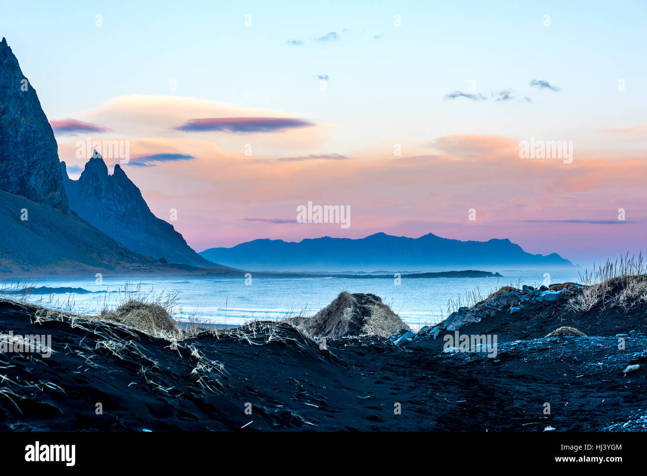 Eine vulkanische Sandstrand in Island gegen die schroffen Berge und einen schönen Pastell Sonnenuntergang als Tag schlüpft in Nacht gerahmt. Stockfoto