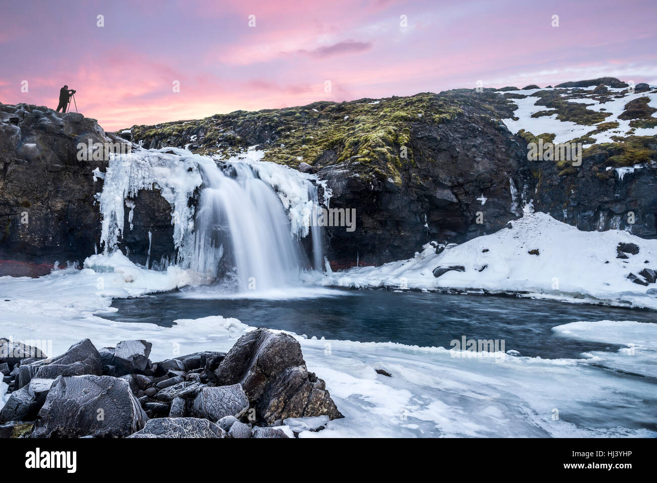 Ein kalten verschneiter Wasserfall im Hochland von Island umrahmt von Pastell Himmel und zerklüftete Gelände bietet landschaftlich Inbegriff der gefrorenen Wildnis Stockfoto
