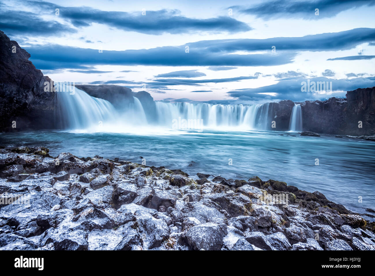 Godafoss Wasserfall bei Sonnenaufgang zeigt das Wasser in Strömen über die Kante und kicking eine neblige Wolke über dem Wasser mit Schnee bedeckt die Klippen. Stockfoto
