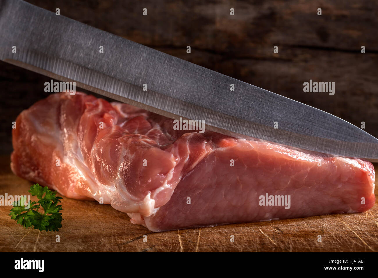 Schneiden von rohem Schweinefleisch Muskel mit Messer über hölzernen Hintergrund Stockfoto