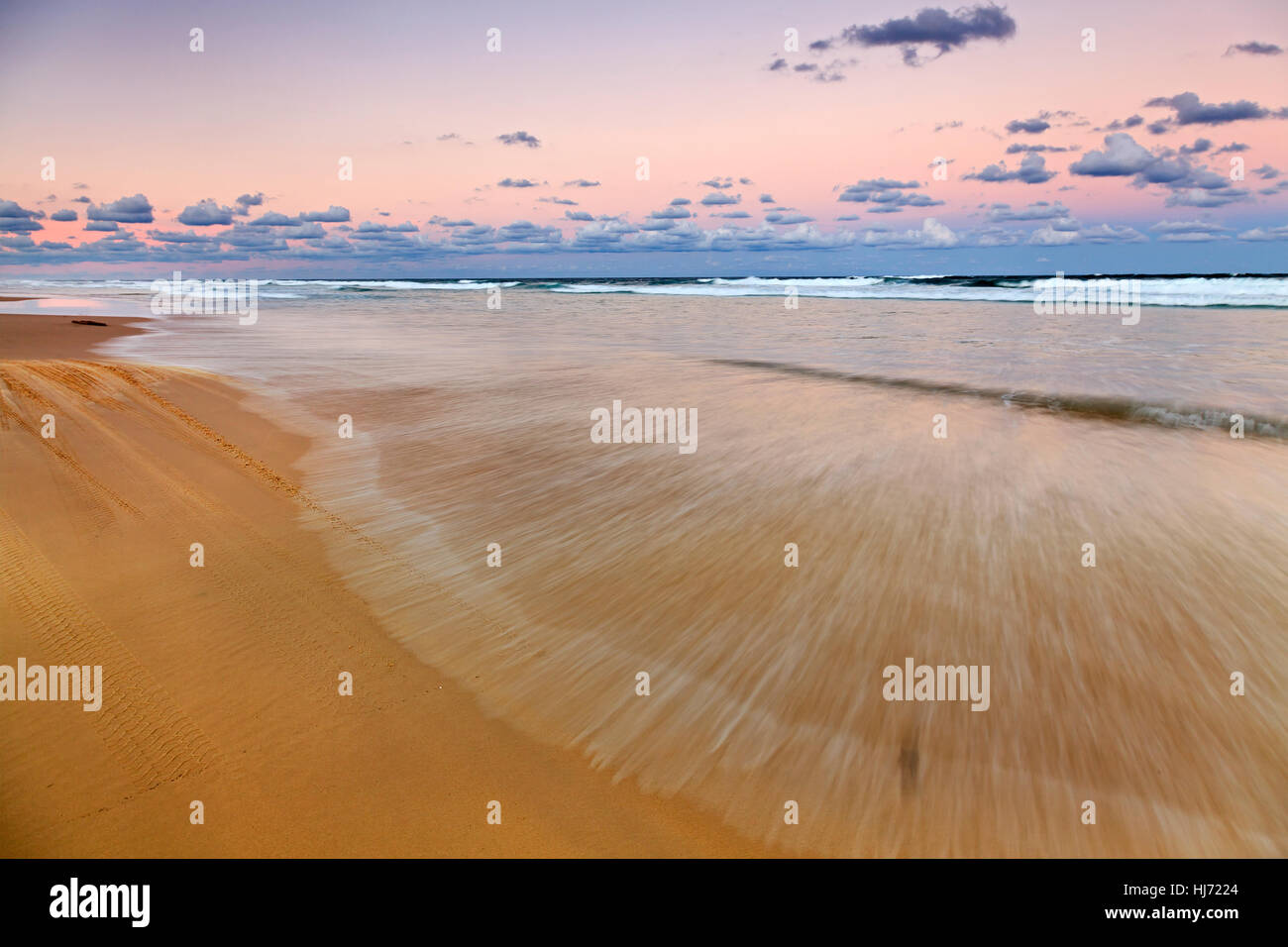 Fraser Island 75 Meilen Strand bei Sonnenuntergang lange Exposition verschwommen Wellen und Gezeiten über flachen Sandstrand in Australien, Queensland. Stockfoto