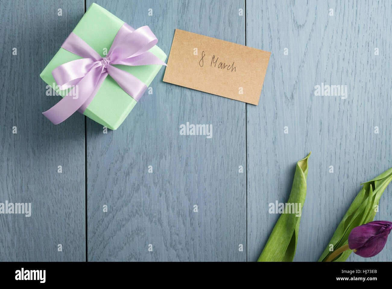 grüne Geschenkbox auf blauen Holztisch mit Papier-Karte für den 8. März Stockfoto