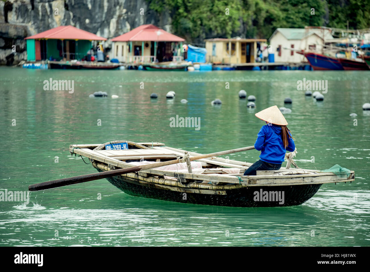 Frau aus Holz Ruderboot Rudern und schwimmende Häuser, Vung Vieng fishing Village, Ha Long Bucht, Bai Tu Long Sektor, in der Nähe von Ha Long, Vietnam Stockfoto