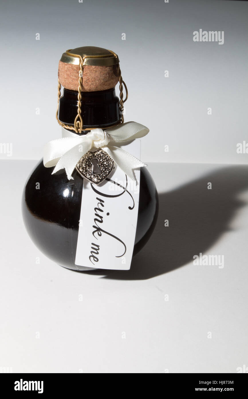 Eine kleine Flasche traditionell hergestellte Schaumwein aus grau- und Feder, beschriftet "Trink mich" mit Herz Charme angebracht. Stockfoto