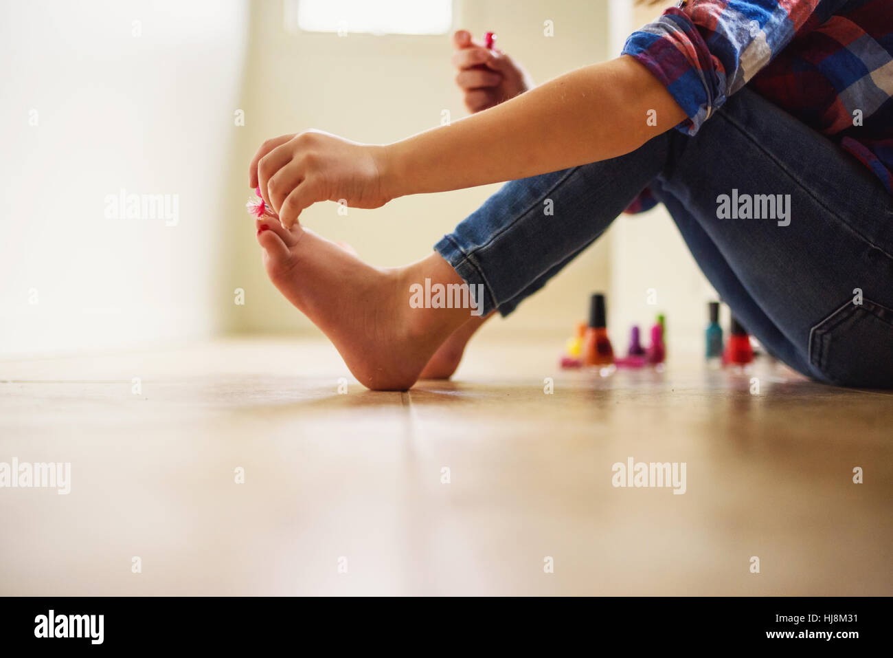 Ein junges Mädchen, das auf dem Boden sitzt und ihre Zehennägel mit Nagellack bemalt Stockfoto