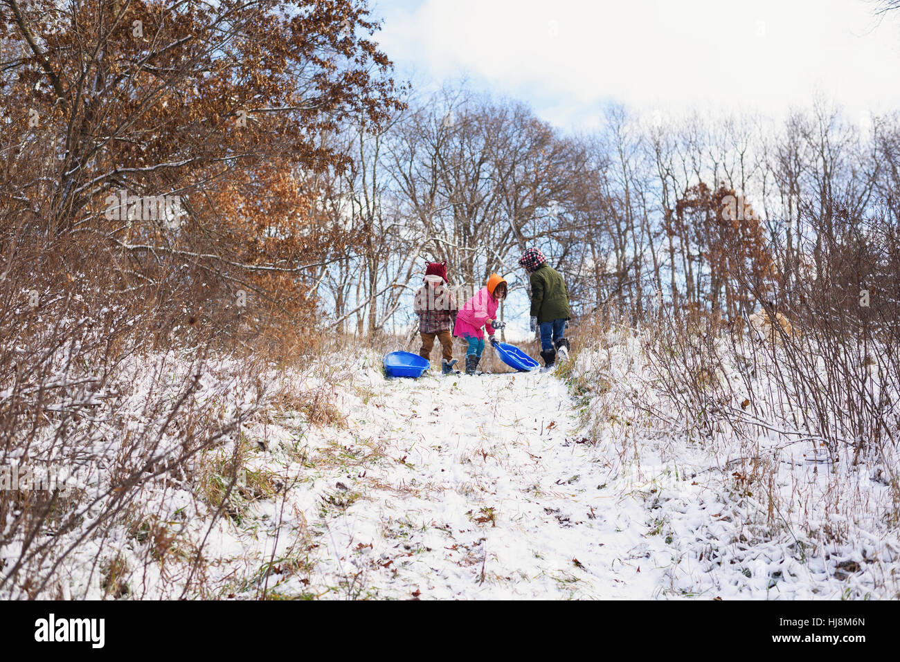 Drei Kinder mit Schlitten stehen an der Spitze eines Hügels Stockfoto