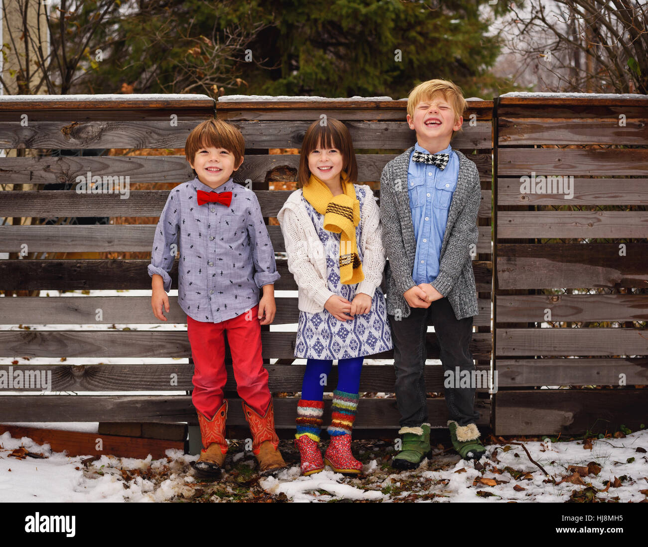Drei glückliche Kinder, die durch einen Zaun im Garten stehen Stockfoto