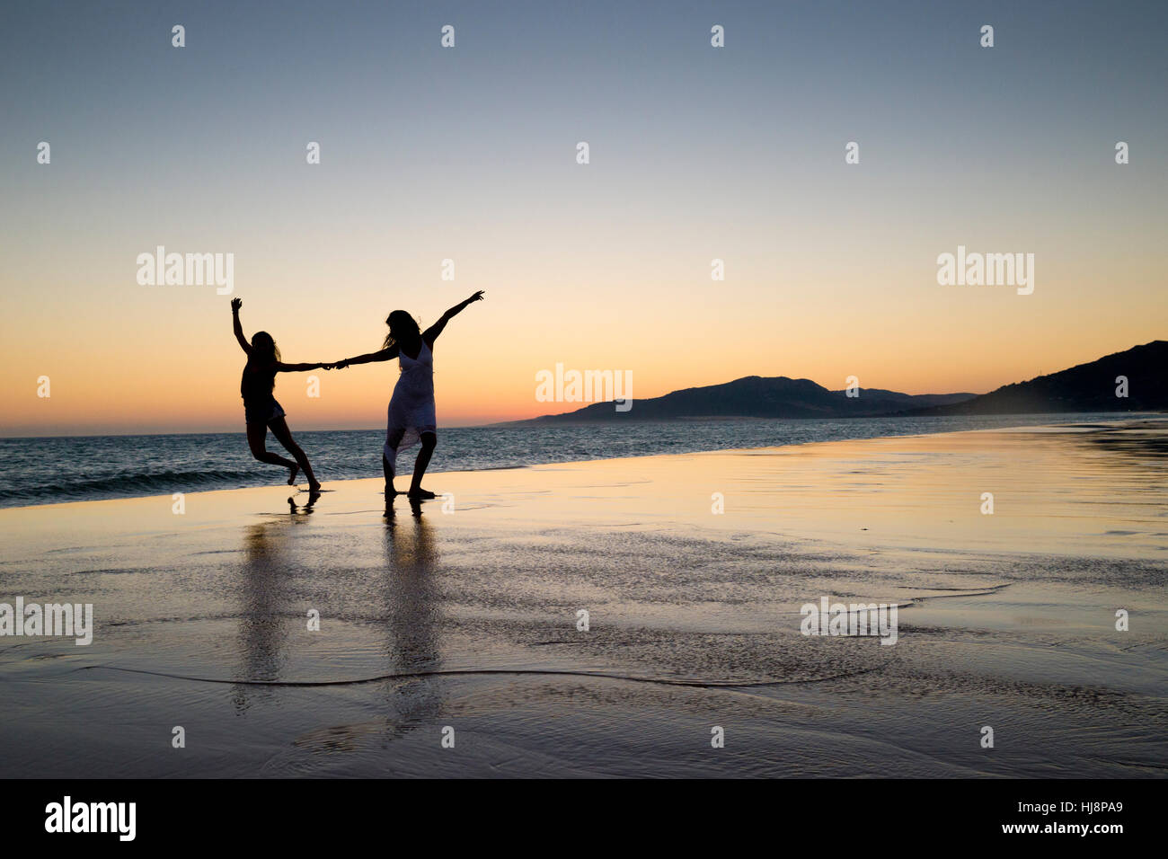 Silhouette der beiden Frauen tanzen auf Los Lances Strand bei Sonnenuntergang, Tarifa, Cádiz, Andalusien, Spanien Stockfoto