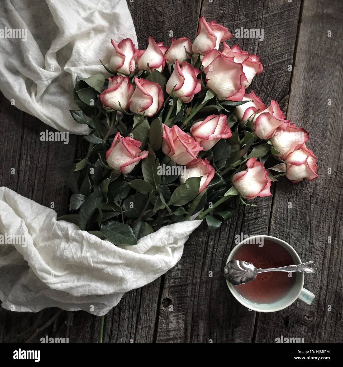 Bukett von Rosen und eine Tasse Tee mit einem weißen Schal Stockfoto