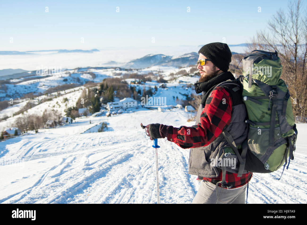 Bärtige Backpacker auf dem schneebedeckten Berg stehend Stockfoto