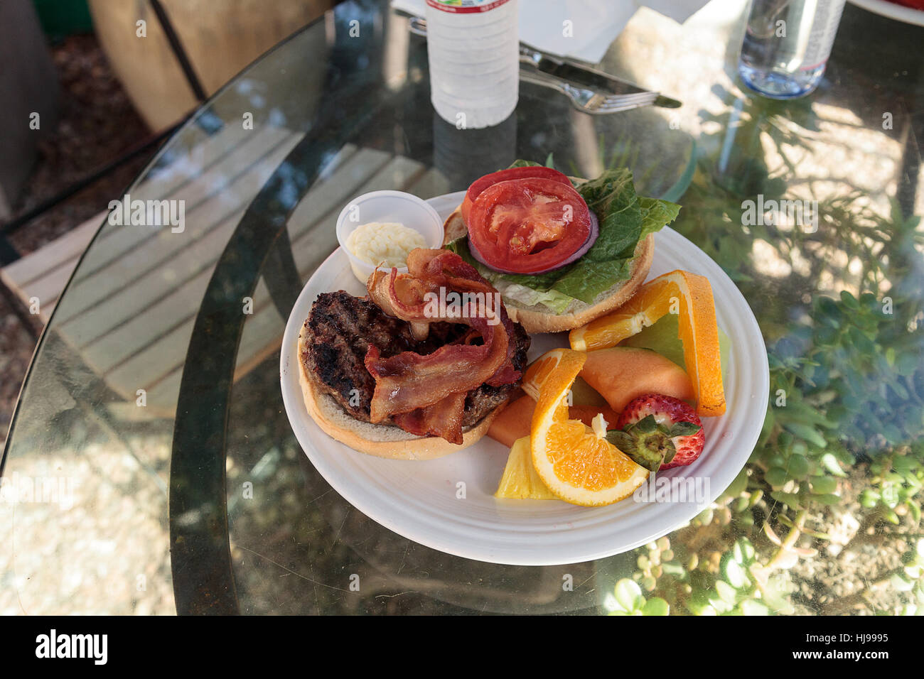 Hamburger mit Speck an der Spitze auf einem flauschigen Brot Brötchen und einer Seitenlänge von Obst wie Orangen, Erdbeeren, Melone und Ananas für l Stockfoto