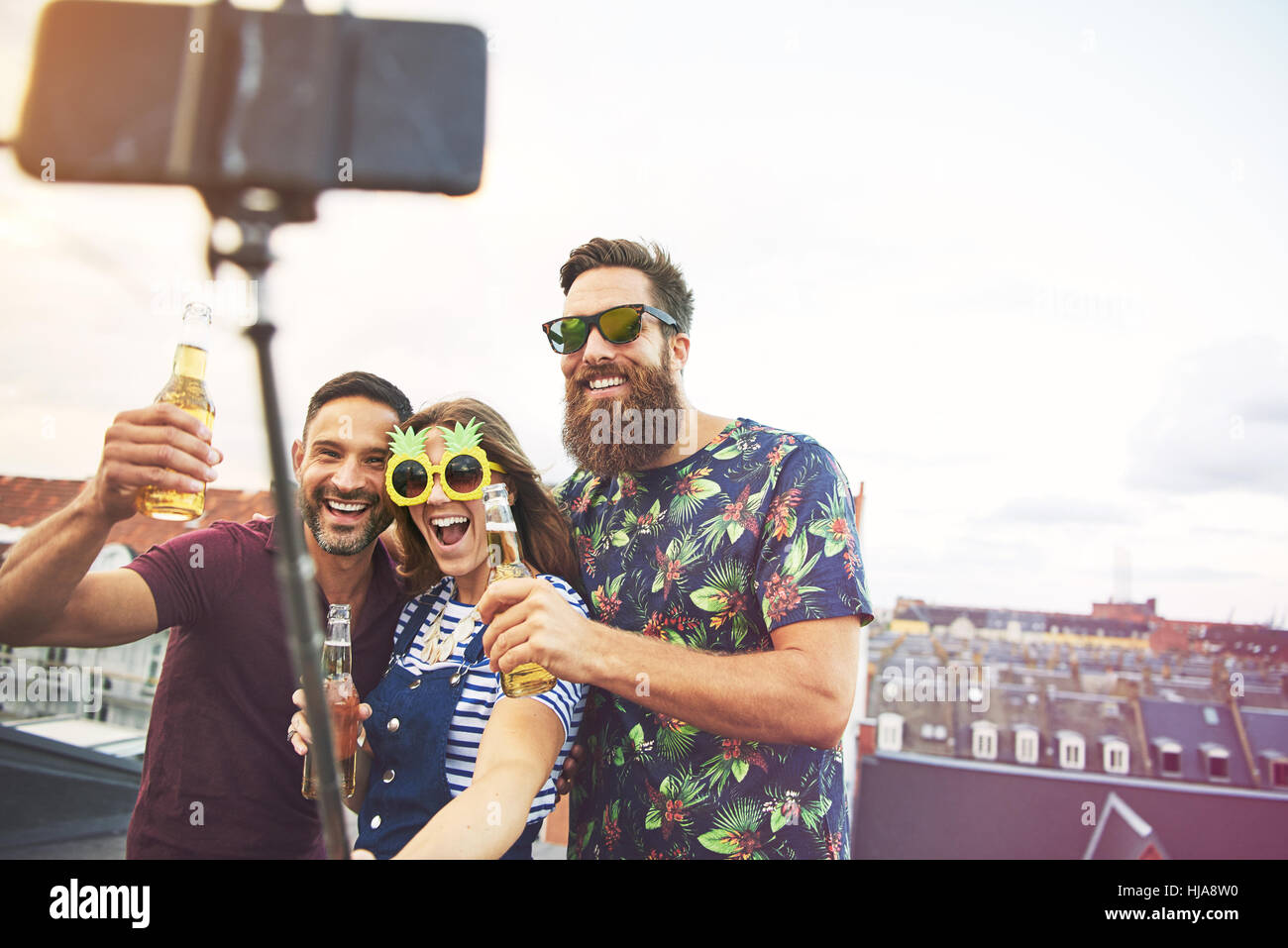 Drei inebriated männlichen und weiblichen Freunde, die Bilder von sich mit selfie stick Kamera Handy auf dem Dach Stockfoto