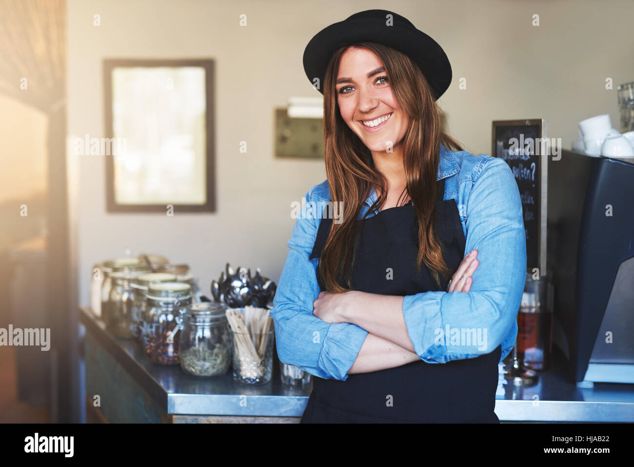 Hübsches Mädchen in schwarzen Hut und Schürze posiert mit Hände gekreuzt und lächelnd in die Kamera im Café. Stockfoto