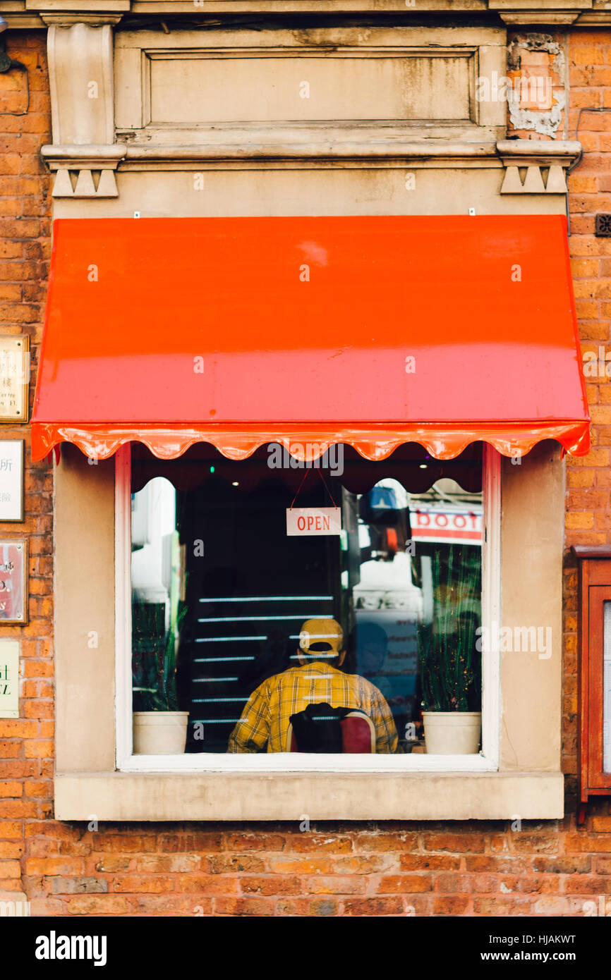 Restaurant-Fenster gesehen von außen mit einer Person in gelb, die drinnen sitzen Stockfoto