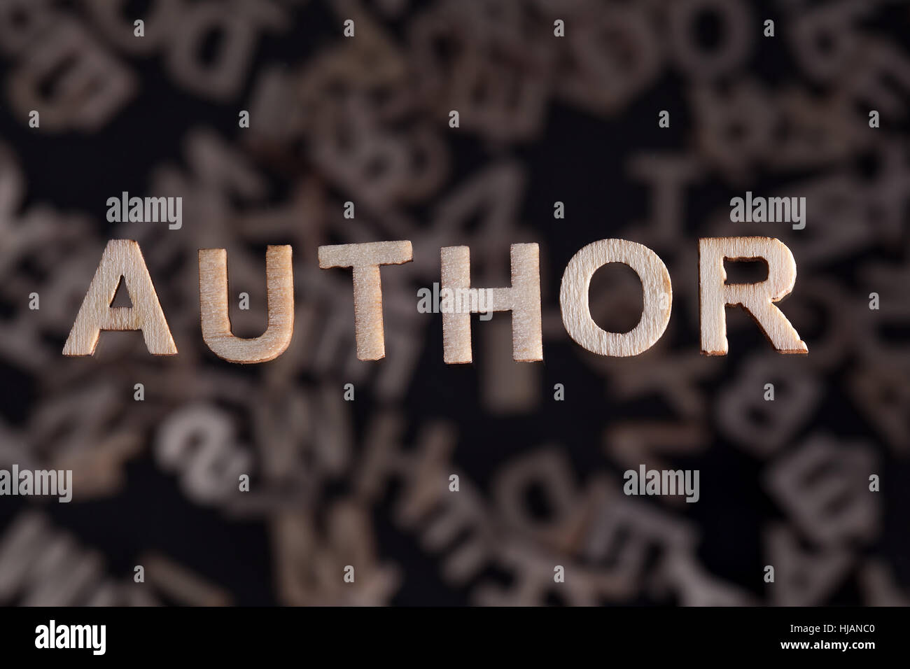 Autor Holzbuchstaben Holz schwebt über zufällige Buchstaben unten außerhalb des Fokus auf einem schwarzen Hintergrund gegründet Stockfoto
