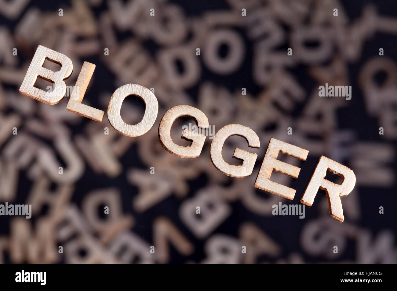 Blogger Holz Buchstaben Text in Holz schweben über zufällige Buchstaben außerhalb des Fokus auf einem schwarzen Hintergrund erstellt Stockfoto