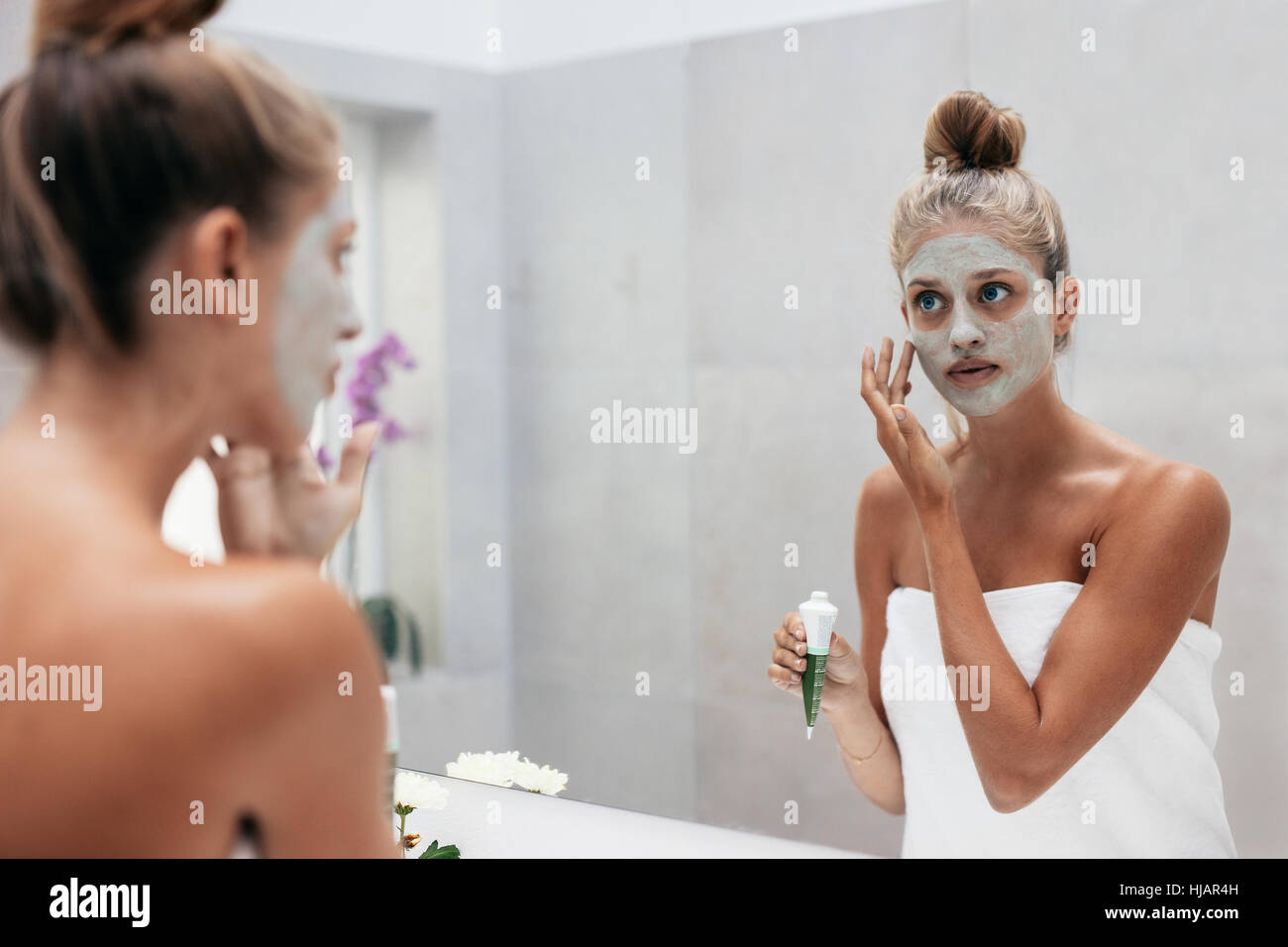 Weibchen mit kosmetischen Maske auf Gesicht im Badezimmer. Junge Frau Gesicht Maske vor Spiegel. Stockfoto