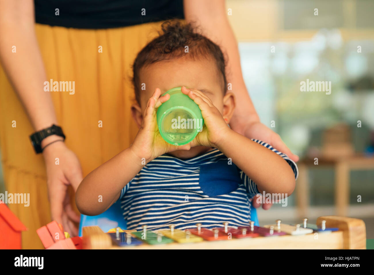 Glückliches Baby Wasser trinken und spielen mit Spielzeug Blöcke im Kindergarten. Stockfoto